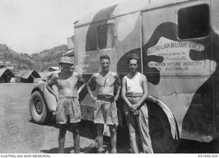 PORT MORESBY, PAPUA, 1942-1943. SERGEANT GEORGE ARKLESS (CENTRE) WITH TWO COMPANIONS STANDING BESIDE THE FORD TRUCK OF MOBILE CINEMA UNIT NO. 76, AUSTRALIAN ARMY AMENITIES SERVICE. (DONOR: G. ..