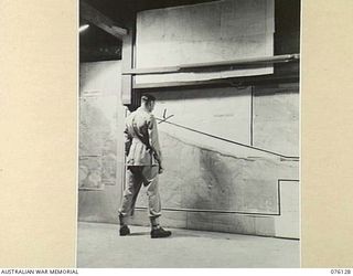 LAE, NEW GUINEA. 1944-09-14. NX104311 CAPTAIN F.B. JOHNSON, EXAMINING POSITIONS ON A MPA IN THE BATTLE ROOM, HEADQUARTERS NEW GUINEA FORCE