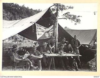 WEWAK POINT, NEW GUINEA. 1945-08-30. MEMBERS OF A AND B COMPANIES, 2/3 MACHINE-GUN BATTALION, READING AND RESTING OUTSIDE THE YMCA CENTRE WHICH IS PROVIDED WITH SUPPLIES BY THE AUSTRALIAN COMFORTS ..