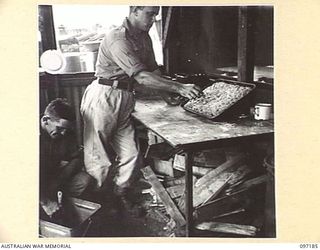 CAPE WOM, NEW GUINEA. 1945-09-27. PRIVATE G.A. VAN BAEL (1), EXAMINING A CAKE WHILE HIS ASSISTANT PRIVATE A.H. MCDONALD (2), PREPARES THE MIDDAY MEAL AT THE COOKHOUSE OF 110 BRIGADE ORDNANCE FIELD ..