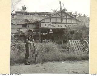 MADANG, NEW GUINEA. 1944-04-24. THE WAREHOUSE OF BURNS, PHILP & CO., LTD., WHICH WAS USED BY JAPANESE FORCES AS A STOREHOUSE AND NOW SHOWS THE EFFECTS OF RAAF BOMBING. THE SOLDIER AT THE ..