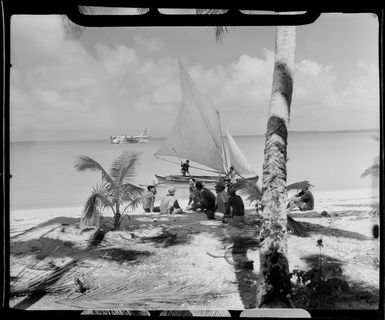 Locals on beach, Akaiami, Aitutaki, Cook Islands, including sail boat and TEAL (Tasman Empire Airways Limited) Flying boat in the distance