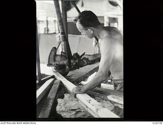NADZAB, NEW GUINEA. C. 1944-02. CORPORAL A. L. GRIFFIN, COLLINGWOOD, VIC, AND NO. 62 MOBILE WORKS SQUADRON RAAF, OPERATING A COMPRESSED AIR SAW TO CUT BUSH-GROWN TIMBER FOR ROOF TRUSSES FOR OFFICE ..