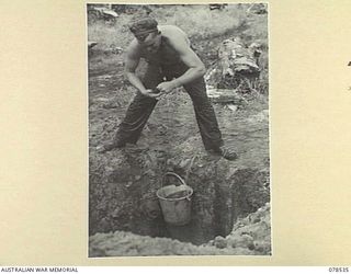 BOUGAINVILLE ISLAND, 1945-01-20. NX194754 PRIVATE A.J. WILCOCKSON "A" COMPANY, 42ND INFANTRY BATTALION DRAWING WATER FROM A WELL SUNK IN THE COMPANY AREA IN MAWARAKA VILLAGE