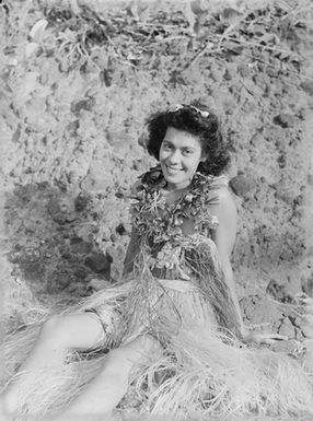 [A young Polynesian woman sitting on coastal rocks]