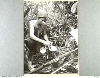 1943-07-31. ALLIED CAPTURE OF MUBO. IN A LITTLE CLEARED SPACE IN THE JUNGLE FIRST CLASS PTE. WILLIAM HATTAN, OF OREGON CITY, OREGON, COOKS HIS LUNCH DURING THE ALLIED ADVANCE ON MUBO, IN THE ..