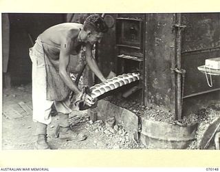 DUMPU, NEW GUINEA. 1944-02-05. QX52385 PRIVATE E.A. EDGEWORTH (1) OF THE 57/60TH INFANTRY BATTALION, REMOVING BREAD ROLLS FROM AN AMERICAN FIELD OVEN AT THE 15TH INFANTRY BRIGADE BAKERY