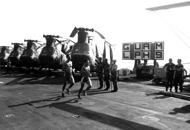 Aviation Bostswain's Mate fuels 3rd Class (ABF3) J. Deshaies and Corporal R. Perez run past a row of CH-46 Sea Knight helicopters and a Sea Sparrow launcher on the USS GUAM (LPH 9), They are the final runners in the trans-Atlantic marathon to honor the Olympic spirit. The race began 4/20 in Rota, Spain, and ended 5/1 inside the 3-mile limit near Morehead City, North Carolina