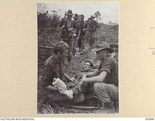 YAMIL AREA, NEW GUINEA, 1945-07-08. PTE R.L. PICONE, D COMPANY, 2/5 INFANTRY BATTALION, BEING ATTENDED BY MATES AFTER BEING ACCIDENTALLY WOUNDED IN THE FOOT DURING THE ADVANCE TO ULUPU TO TAKE UP A ..