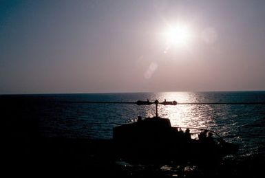 A silhouetted right side view of a Marine AH-1 Sea Cobra helicopter on the flight deck of the amphibious assault ship USS GUAM (LPH 9) during operations off the coast of Beirut, Lebanon