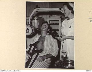 LAE AREA, NEW GUINEA. 1945-08-11. AN X-RAY BEING TAKEN OF WARRANT OFFICER SMITH'S (1), SWOLLEN JAW BY MAJOR B.J. MAHON, DENTAL OFFICER, 2/7 GENERAL HOSPITAL (NOT SHOWN), ASSISTED BY PRIVATE E.C. ..