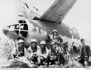 1943-01-08. PAPUA. BUNA. THIS PICTURE IS EVIDENCE OF THE ACCURACY OF ALLIED AIRMEN WHEN THEY BOMBED THE AIRSTRIP AT BUNA. PICTURE SHOWS ALLIED SOLDIERS GROUPED ROUND A DAMAGED JAP BOMBER. (NEGATIVE ..