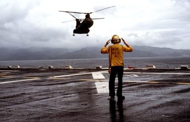 A flight deck crewman signals a CH-46 Sea Knight helicopter approaching to land aboard the amphibious assault ship USS GUAM (LPH 9), during Operation URGENT FURY off the coast of Grenada