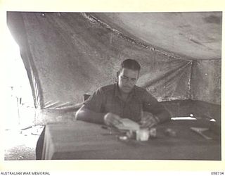 CAPE WOM, NEW GUINEA. 1945-11-14. MAJOR J.J. MCWILLIAMS, DEPUTY ASSISTANT PROVOST MARSHAL, 6 DIVISION PROVOST COMPANY, AT WORK IN HIS OFFICE