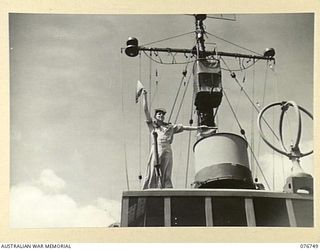 LANGEMAK BAY, NEW GUINEA. 1944-10-23. A SIGNALLER SEMOPHORING A MESSAGE FROM THE RAN CORVETTE, GYMPIE