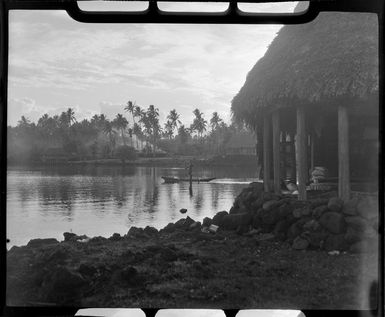 Unidentified man in a canoe at Faleolo, Apia, Upolu, Samoa, shows fales and palm trees