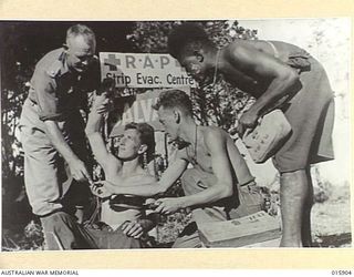 1943-10-02. NEW GUINEA. MARKHAM VALLEY. A MEDICAL OFFICER FROM N.S.W. ATTENDS A WOUNDED VICTORIAN SOLDIER WHILE PTE. V. GILBERT OF RANDWICK, N.S.W. AND MANAZE A MARKHAM VALLEY NATIVE, ASSIST HIM. ..