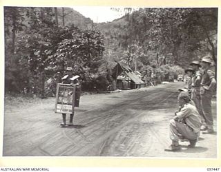 RABAUL, NEW BRITAIN. 1945-10-03. A JAPANESE SOLDIER WITH A VICTORY LOAN SANDWICH BOARD, WALKING AROUND HEADQUARTERS 11 DIVISION AREA TO HELP PROMOTE VICTORY LOAN CONTRIBUTIONS FROM THE TROOPS