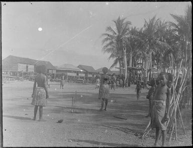 Women playing cricket with a totem pole platform in background, Papua, ca. 1923 / Sarah Chinnery