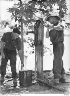 ALEXISHAFEN, NEW GUINEA. 1944-05-16. VX61632 PRIVATE C JENNINGS (1), AND VX26926 LANCE CORPORAL J REYNOLDS (2), MEMBERS OF THE 2/15TH FIELD AMBULANCE, USING THE PUMP AT THE OLD CATHOLIC MISSION TO ..