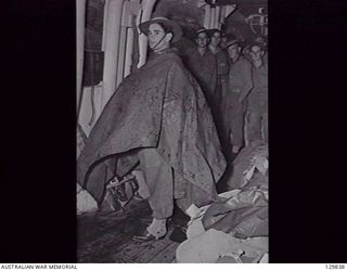 DARLING HARBOUR, NSW. 1946-06-21. SX38744 PRIVATE H. H. ATWELL BOUND FOR PORT PIRIE, ADELAIDE, PUTS ON A ONE MAN TENT TO KEEP THE RAIN OFF WHILE WAITING TO DISEMBARK FROM HMAS MANUNDA, AFTER ITS ..