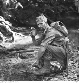 PAPUA, NEW GUINEA. 1942-10. PRIVATE H.E. NEWMAN OF THE 2/33RD AUSTRALIAN INFANTRY BATTALION STOPS BY FOR A DRINK DURING A PATROL BETWEEN NAURO AND MENARI