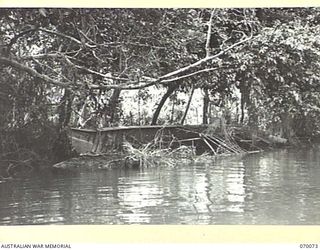 GOALING RIVER AREA, WEST NEW GUINEA. 1944-01-25. A JAPANESE BARGE ABANDONED BY THE RETREATING ENEMY LYING UNDER THE SHELTER OF OVERHANGING TREES ON THE BANKS OF GOALING RIVER, AND PARTIALLY ..