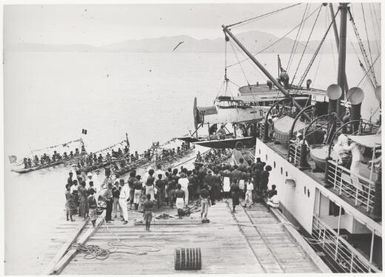 A crowd of people, some in canoes, watching the unloading of a Short Shrimp seaplane, G-AUPZ, from a ship, Port Moresby, Papua New Guinea, 1922 / Frank Hurley