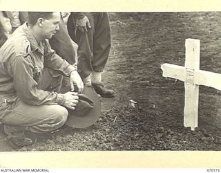 DUMPU, NEW GUINEA. 1944-02-06. QX30576 PRIVATE L.F. ADKINS (1) OF THE 2/12TH INFANTRY BATTALION, READING AN INSCRIPTION ON ONE OF THE NEAT WHITE CROSSES AT DUMPU WAR CEMETERY