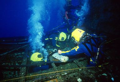 Four helmeted Navy divers with air hoses to the surface work to raise the hull of the submarine ex-USS BLUEGILL (SS-242) during Pacific Submarine Salvage Exercise 83 (PACSUBSALVEX-83) off the coast of Maui