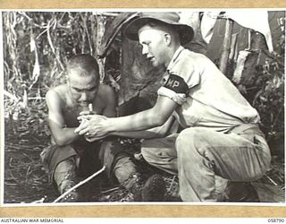 DUMPU, NEW GUINEA, 1943-10-10. NX74107 CORPORAL H.J. MURRAY OF THE 7TH AUSTRALIAN DIVISION PROVOST COMPANY LIGHTING A CIGARETTE FOR A JAPANESE PRISONER, AT HEADQUARTERS, 21ST AUSTRALIAN INFANTRY ..