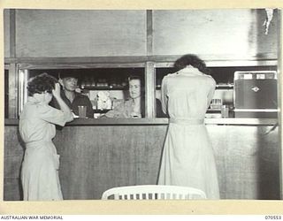 PORT MORESBY, PAPUA, 1944-02-20. MEMBERS OF THE AUSTRALIAN ARMY MEDICAL WOMEN'S SERVICE PURCHASING GOODS FROM THE CANTEEN IN THE AUSTRALIAN WOMEN'S SERVICES CLUB, CONDUCTED BY THE AUSTRALIAN ARMY ..