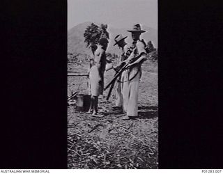 SALAMAUA, NEW GUINEA, 1940-04-?. TWO MEMBERS OF THE NEW GUINEA VOLUNTEER RIFLES (NGVR) AFTER PRACTICE AT THE RIFLE RANGE. A NATIVE POURS BOILING WATER THROUGH A FUNNEL TO CLEAN ONE RIFLE. (DONOR H. ..