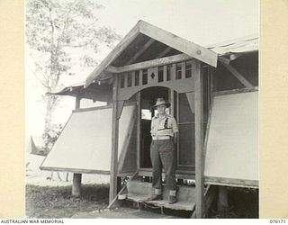 LAE, NEW GUINEA. 1944-09-02. VX104118 MAJOR R.C. UPSON, OFFICER IN CHARGE, 22ND WORKS COMPANY, ROYAL AUSTRALIAN ENGINEERS, STANDING OUTSIDE A HUT ERECTED BY MEMBERS OF HIS UNIT AND PRESENTED TO HIM ..