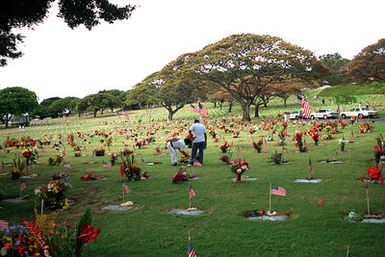 Two visitors place flowers on a grave at the National Memorial Cemetery of the Pacific, also known as the Punchbowl, in observance of Memorial Day. A flag and a flower lei have been placed on each grave in the cemetery by area Boy Scouts.