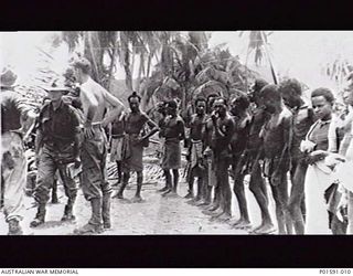 MARKHAM RIVER AREA, NEW GUINEA. C.1945. NATIVE CARRIERS AND MEMBERS OF THE MOBILE PROPAGANDA UNIT, FAR EASTERN LIAISON OFFICE, WAIT IN A VILLAGE FOR SUPPLIES TO BE LOADED. SERGEANT N. (NAT) F. ..