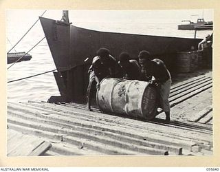 JACQUINOT BAY, NEW BRITAIN, 1945-08-31. NATIVES UNLOADING STORES FROM BARGES OF 53 PORT CRAFT COMPANY ROYAL AUSTRALIAN ENGINEERS