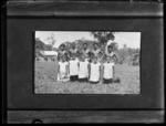 Group of five women kneeling and five men standing in a field with a building in the background.