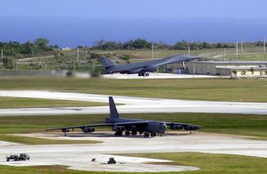 Near a parked US Air Force (USAF) B-52 Stratofortress bomber, a B-1B Lancer Bomber, deployed from Dyess Air Force Base (AFB), Texas, takes off from Andersen AFB, Guam, in support of the 7th Air Expeditionary Wing's mission