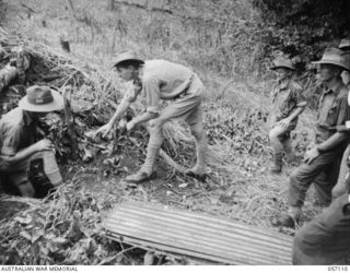 SOGERI VALLEY, NEW GUINEA. 1943-09-19. OFFICERS STANDING BESIDE A CAMOUFLAGED DUGOUT, AT THE NEW GUINEA FORCE TRAINING SCHOOL, TO BE USED FOR THE TEST OF THE PROJECTOR INFANTRY TANK ATTACK MARK 1. ..