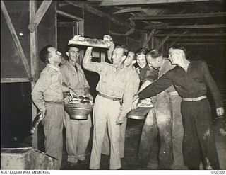 VIVIGANI, GOODENOUGH ISLAND, PAPUA. C. 1943-09. GROUND STAFF OF THE FAMOUS NO. 30 (BEAUFIGHTER) SQUADRON RAAF IN NEW GUINEA RUSH THE COOK WHEN HE PRODUCES A BATCH OF HOT BREAD ROLLS. FROM LEFT: ..