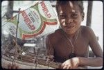 Model canoe with sail made of rice bag, held by smiling boy in Wawela village