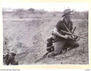 WEWAK AREA, NEW GUINEA, 1945-05-20. SGT W.H. JONES, 2/8 INFANTRY BATTALION (1) AND MR. A. ANDERSON, MOVIE CAMERAMAN (2), TAKING COVER IN A BOMB CRATER. THEY WILL ADVANCE ON ENEMY POSITIONS AT THE ..