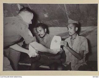 SORAKEN AREA, BOUGAINVILLE. 1945-04-03. SERGEANT H.C. MASTERS, 19 FIELD AMBULANCE (1), ISSUES RED CROSS SOCIETY COMFORTS TO AMBOINESE ESCAPEES AT THE REGIMENTAL AID POST AFTER THEY HAD RECEIVED ..