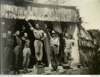 Soputa, New Guinea, 1943. Cast members on the stage of an outdoor theatre giving a fascist salute to an actor portraying Adolf Hitler at a concert given by members of the 36th Battalion, Australian ..