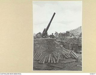 PORT MORESBY, PAPUA. 1942-07. AFTER A HECTIC FEW MINUTES OF ACTION AGAINST JAP BOMBERS IN NEW GUINEA, AUSTRALIAN TROOPS LOOK ROUND FOR MORE TARGETS. SPENT SHELL-CASES CAN BE SEEN IN FRONT OF THE ..