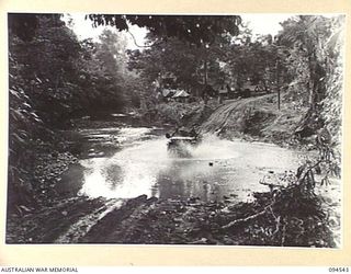 PARCHY RIVER, NEW GUINEA, 1945-07-23. A JEEP AND TRAILER LOADED WITH STORES AND AMMUNITION FOR FORWARD UNITS AT YAMIL SPLASHES ACROSS THE RIVER. THIS DRY WEATHER JEEP ROAD CONSTRUCTED BY 2/14 FIELD ..