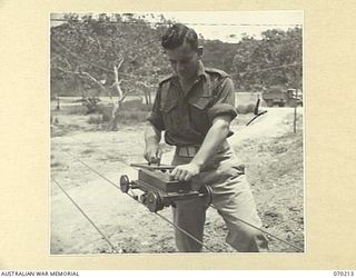 PORT MORESBY, NEW GUINEA. 1944-02-07. NX69134 SIGNALMAN A.E. SPRINGHAM (1) PLACING A MESSAGE IN A CARRIER AT SIGNAL OFFICE, 18TH LINES OF COMMUNICATION SIGNALS. THIS MINIATURE OVERHEAD ELECTRIC ..