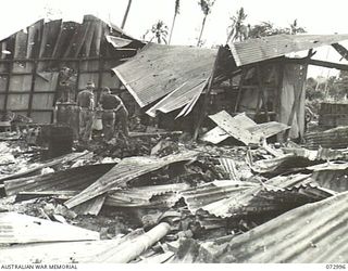 MADANG, NEW GUINEA. 1944-04-25. AUSTRALIAN TROOPS EXAMINE THE BOMB DAMAGE AT A FORMER JAPANESE STORE WHICH CONTAINED MUCH ELECTRICAL EQUIPMENT. THE STORE, SITUATED NEAR THE WATERFRONT WAS GUTTED BY ..