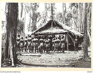 NANTAMBU, NEW BRITAIN. 1945-07-26. NATIVES OF 1 NEW GUINEA INFANTRY BATTALION LINED UP OUTSIDE A HUT AWAITING THEIR TRIAL BY MAJOR COSTELLO, THE DISTRICT OFFICER